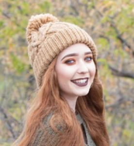 Portait photo d’une femme rousse, portant un bonnet dans un paysage forestier.